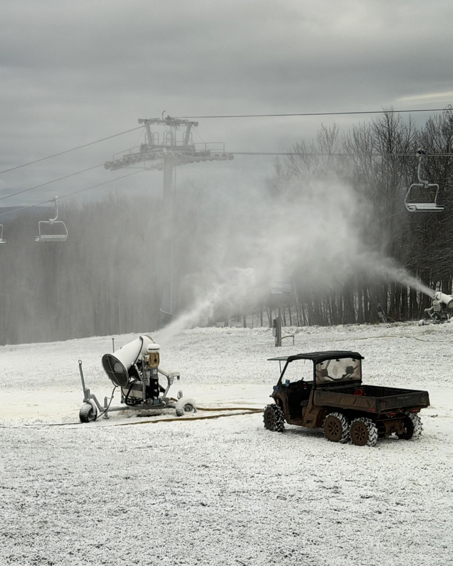 Snow machines and vehicle on a ski slope under gray sky.