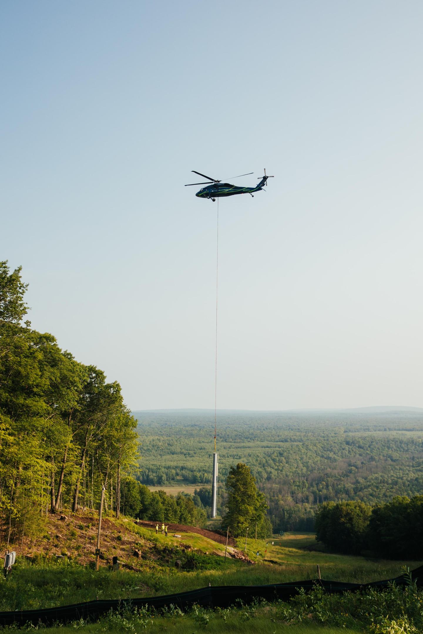Ski lift tower hangs from helicopter before placement on its foundation.