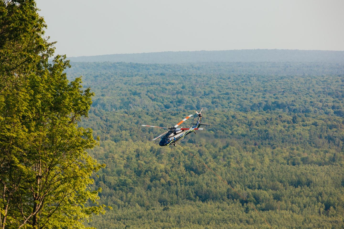 Helicopter turns around over a backdrop of trees and skyline.