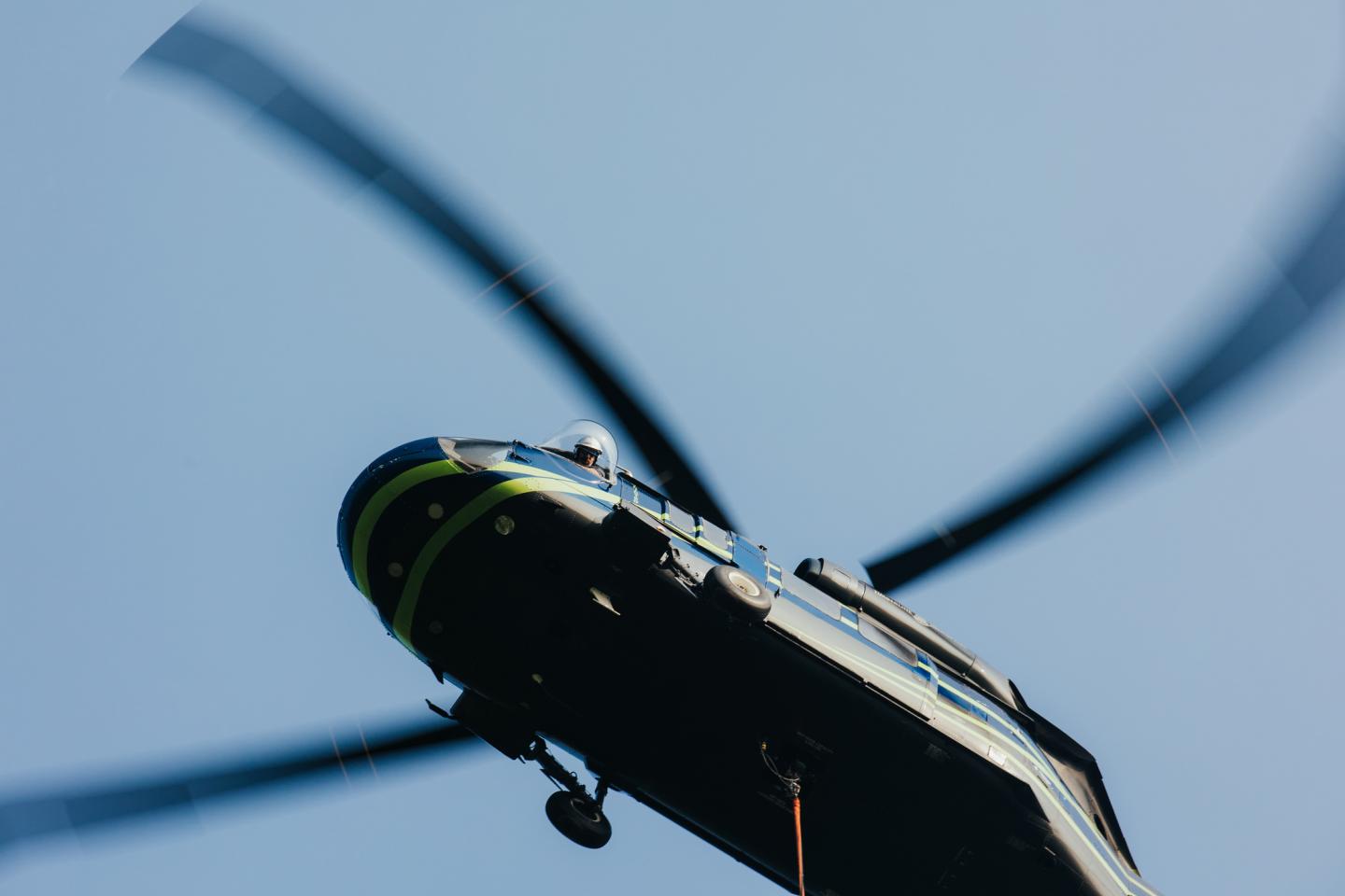 Helicopter pilot looks down through bubble window.