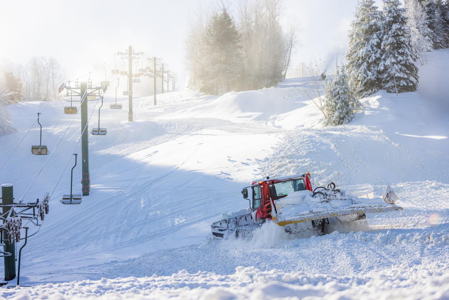 Snowcat pushes snow beneath a chairlift and running snowguns.
