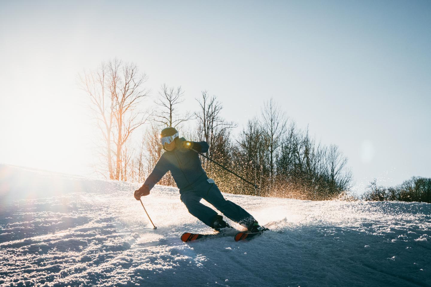 Male skier makes a turn with sun shining in the background.