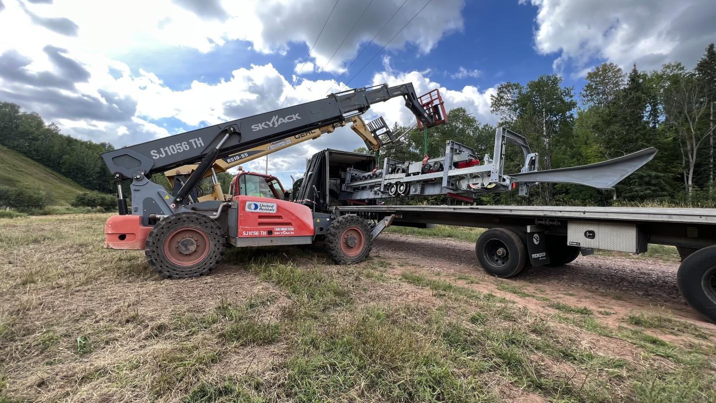 Two forklifts work together to unload a large piece of equipment.