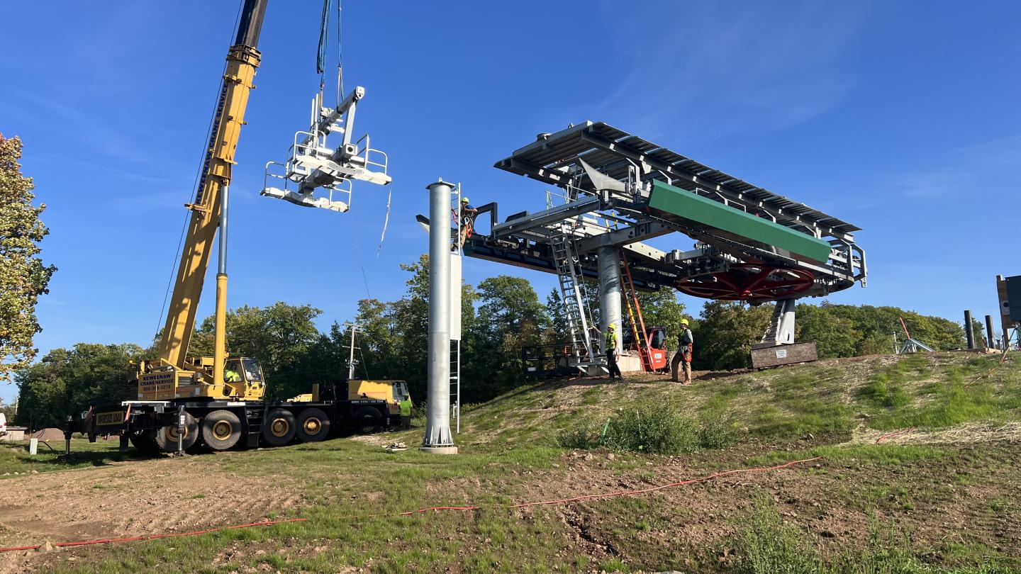 Ski lift tower cross arm is raised into place by crane.