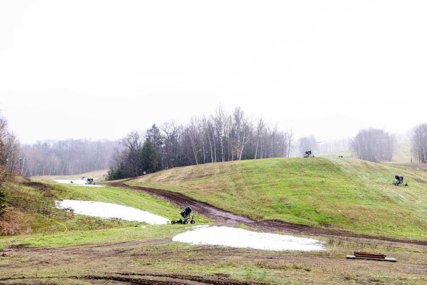 Snowguns staged near piles of melting snow surrounded by green grass.