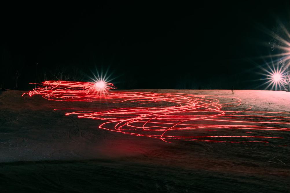 Skiers leave trails of red light in a long exposure photo.