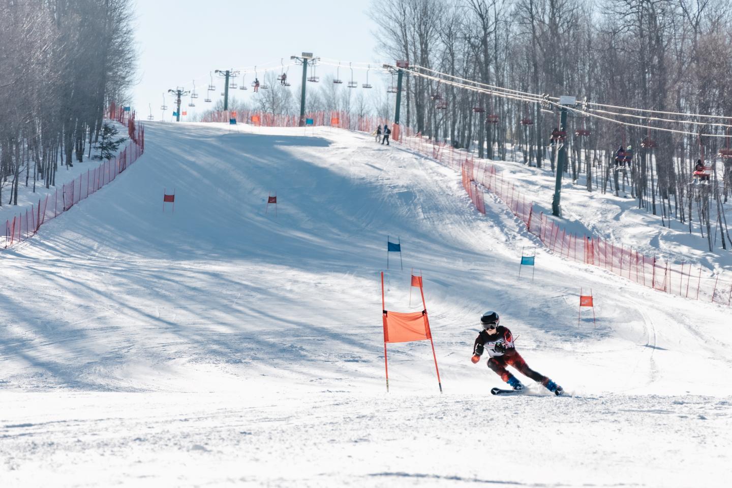 Ski racer passes a gate just beneath a steep section.