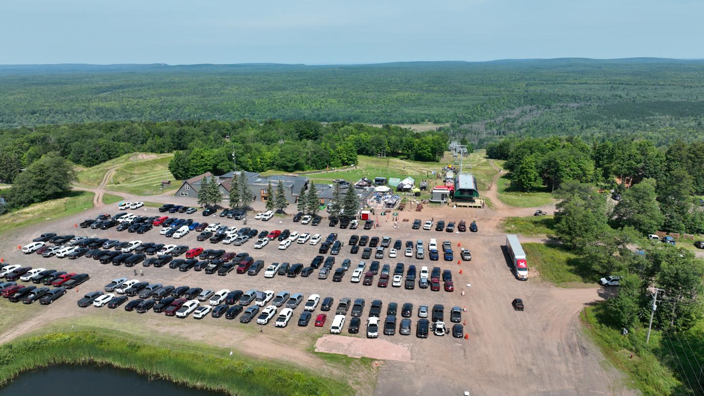 Aerial view of a parking lot with many cars, surrounded by lush green landscape.