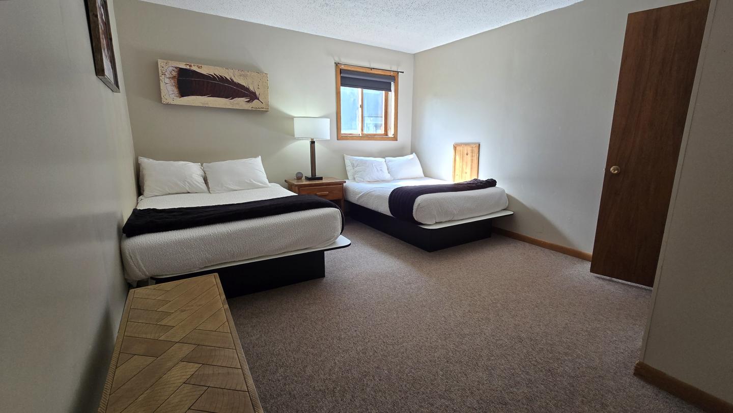 Two beds in a minimalist hotel room with a window and neutral tones.