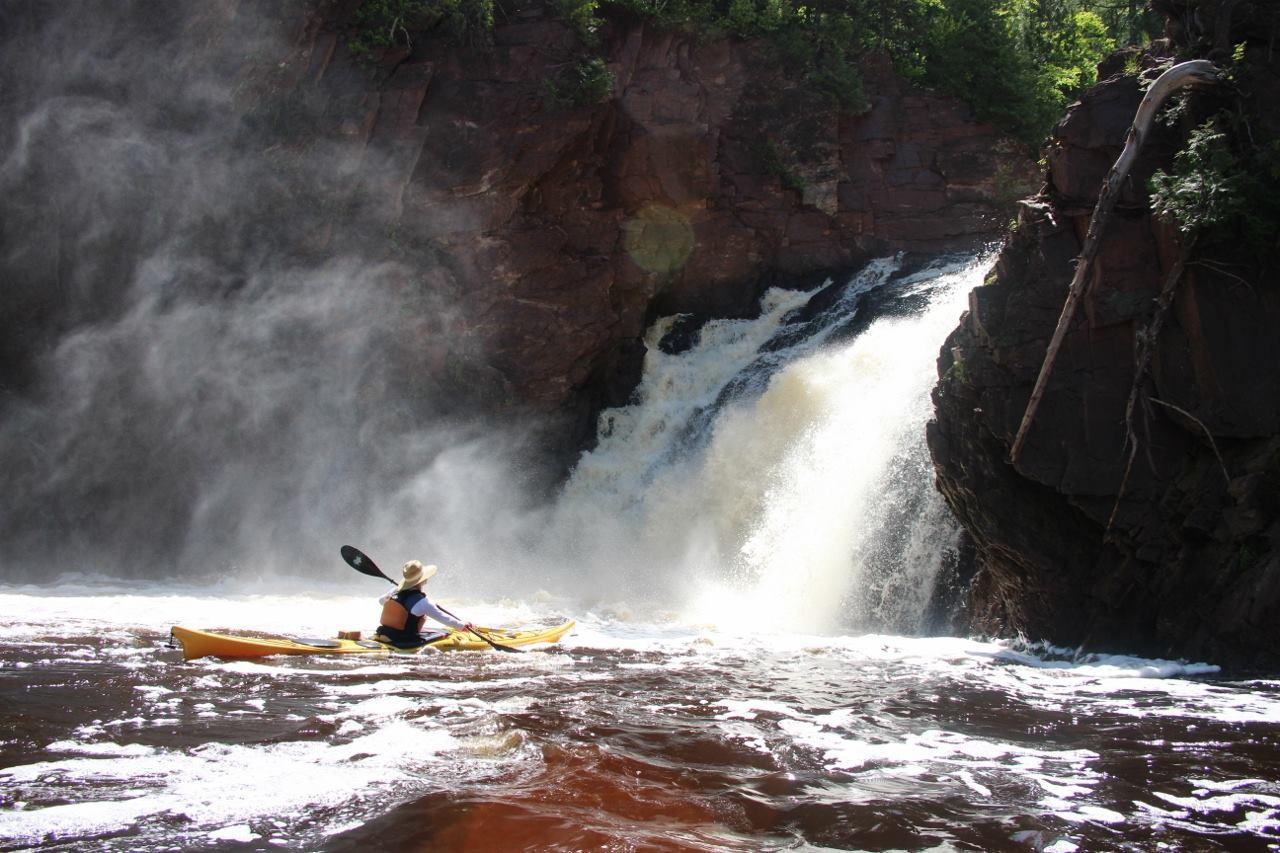 Kayaker paddling near a waterfall with mist and rocky cliffs.