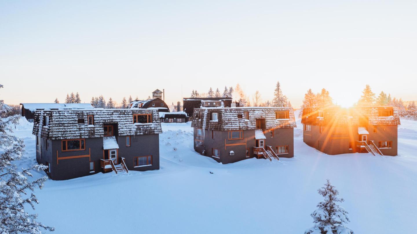 Snowy cabins at sunrise, surrounded by trees.