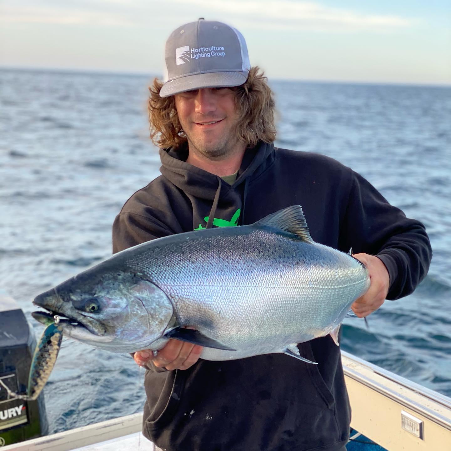 Smiling person holding a large fish on a boat, ocean in background.