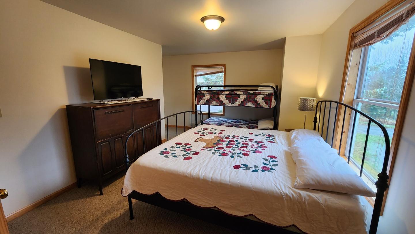 Cozy bedroom with a double bed, bunk bed, dresser, and TV. Natural light from window.