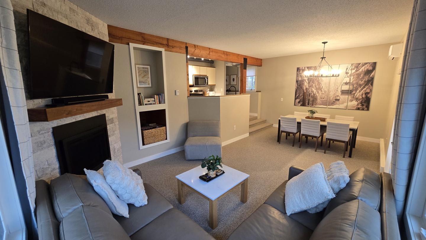 Cozy living room with sofas, wall-mounted TV, dining area, and warm lighting.