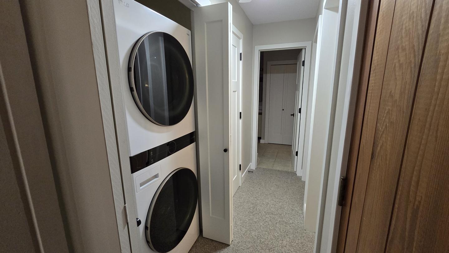 Stacked washer and dryer in a narrow hallway with carpet.