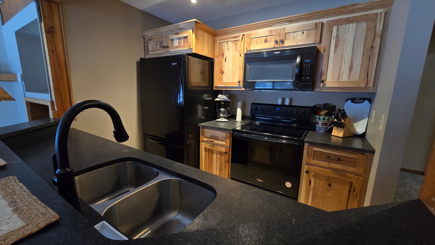 Modern kitchen with wooden cabinets, black appliances, and dual sink.