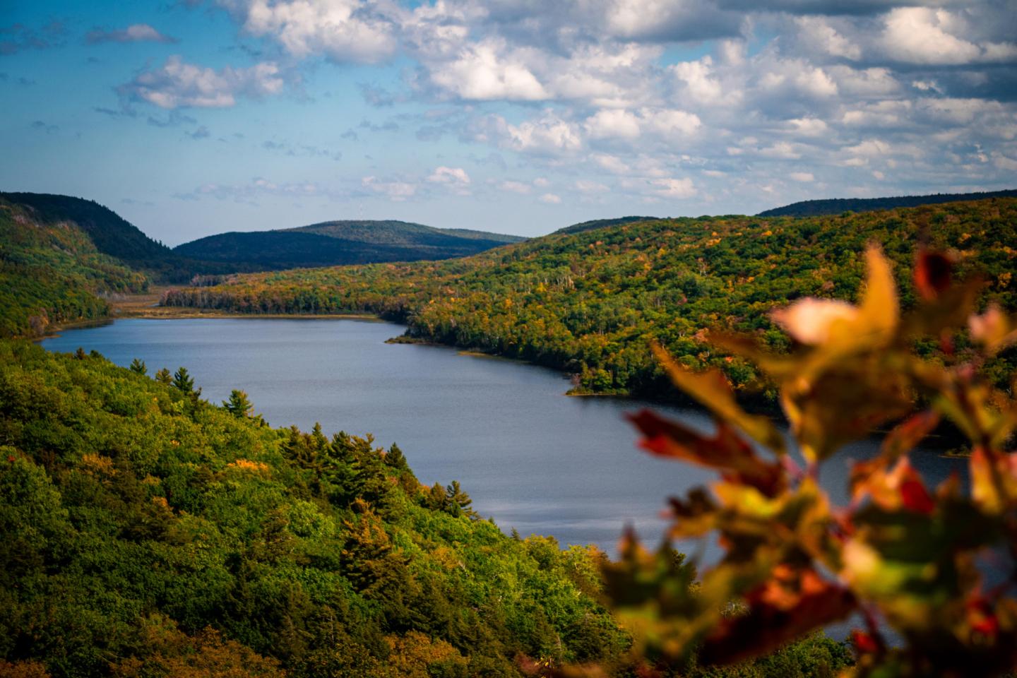 Autumn landscape with a lake, hills, and colorful foliage under a cloudy sky.