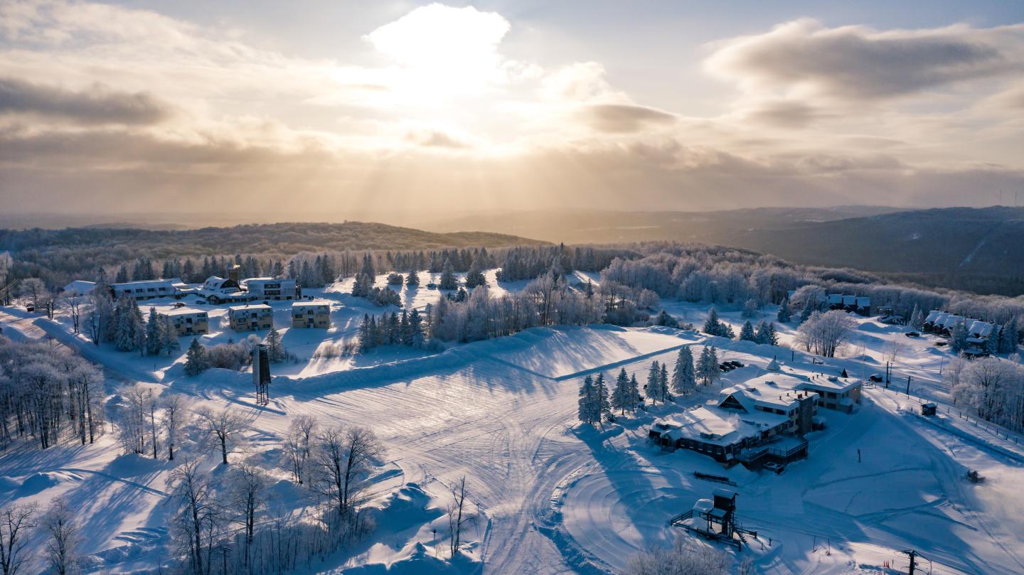 Snowy landscape with buildings and trees under a sunlit sky.