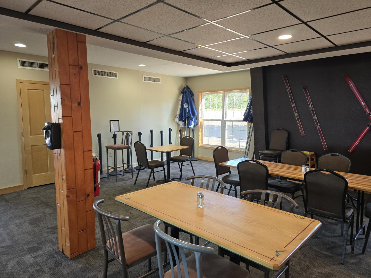 Cozy room with tables, chairs, skis on a wall, and bright window light.