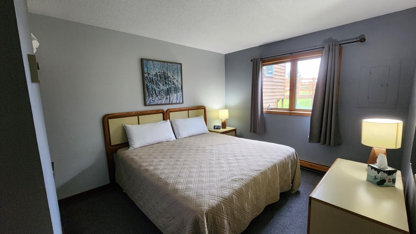 Cozy bedroom with a large bed, bedside lamps, and a window with gray curtains.