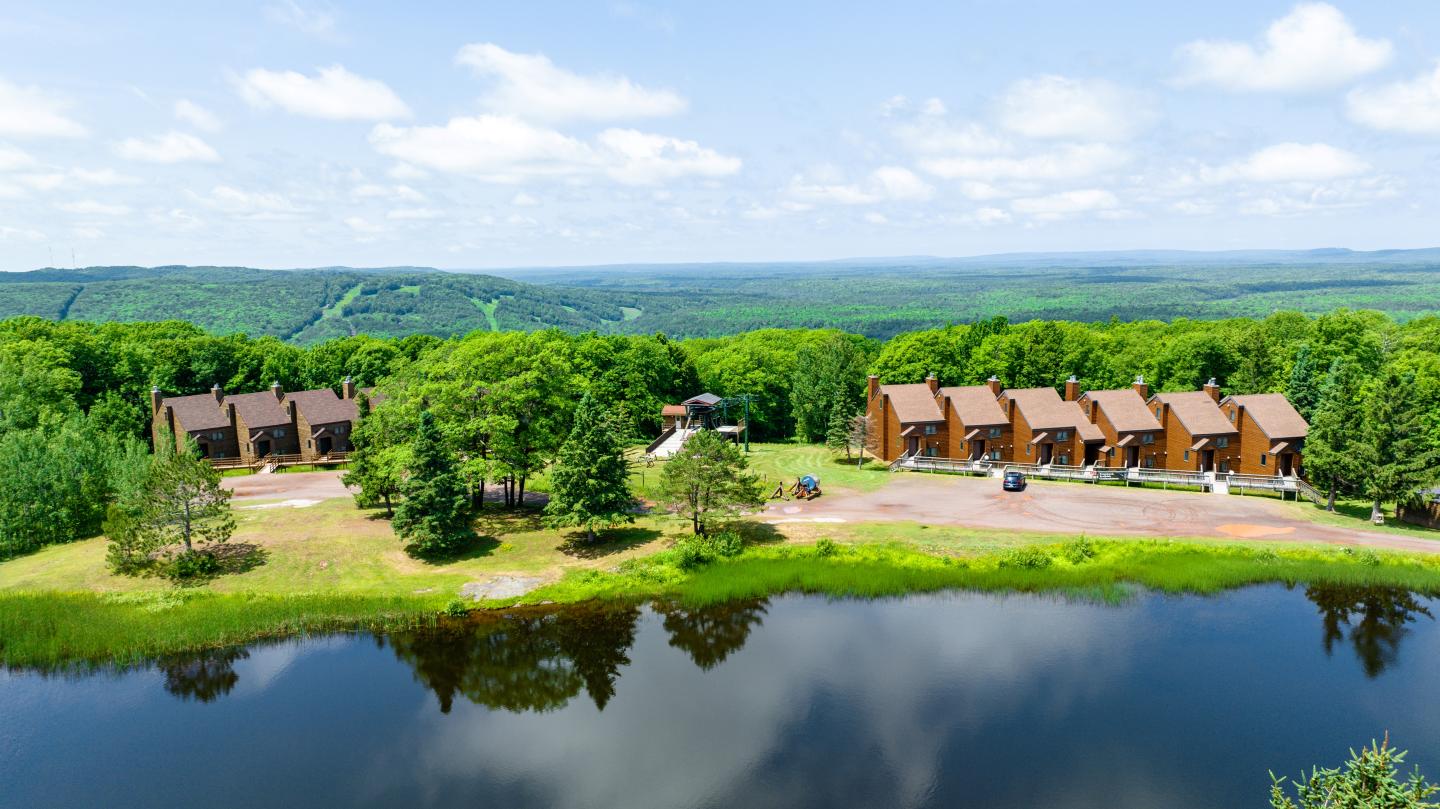 Two clusters of cabins beside a reflective pond, surrounded by lush green trees.