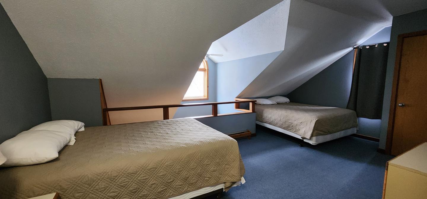 Two beds in an attic room with sloped ceiling and blue carpet.