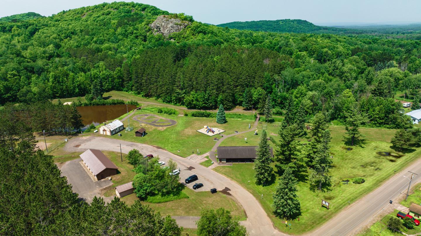 Aerial view of a green landscape with trees, roads, buildings, and distant hills.
