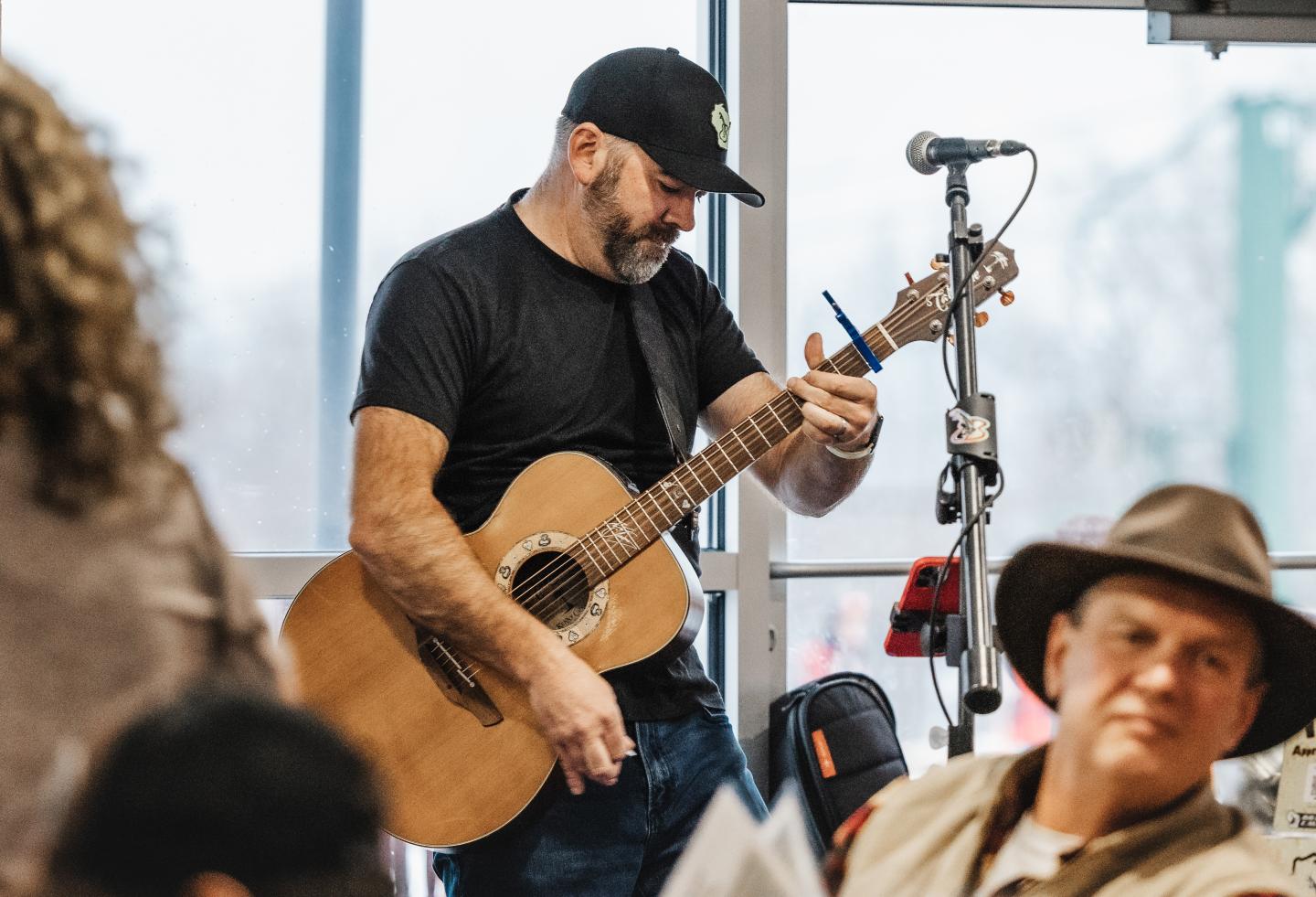 Man playing guitar near a microphone in a casual indoor setting.