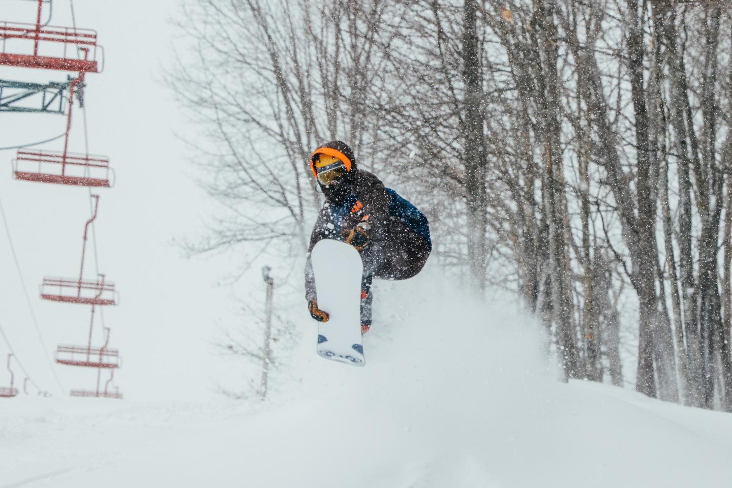 Snowboarder jumping in snowy landscape near trees and ski lift.