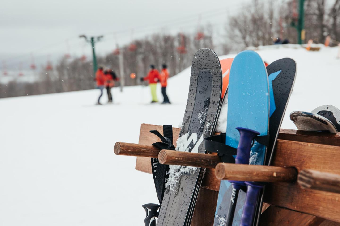 Snowboards resting on a rack, with skiers in the background.