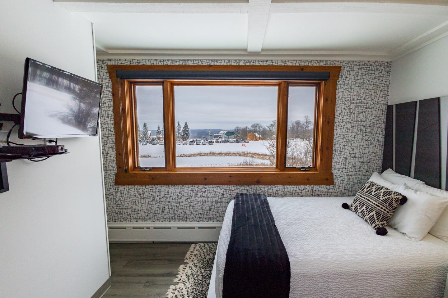 Cozy bedroom with a large window showing snowy landscape.