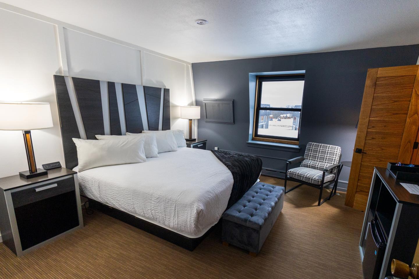Modern hotel room with a king bed, two lamps, and a window with city view.