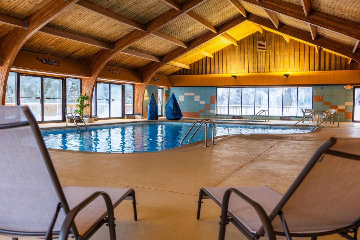 Indoor pool with wooden ceiling, surrounded by lounge chairs.
