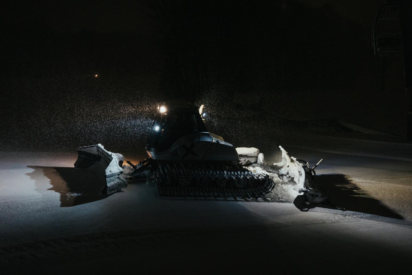 Snowplow clearing snow at night with headlights on.