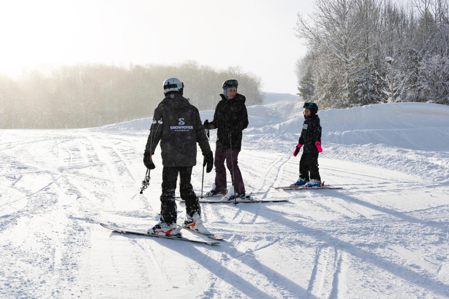 Three people skiing on a snowy trail under a clear sky.