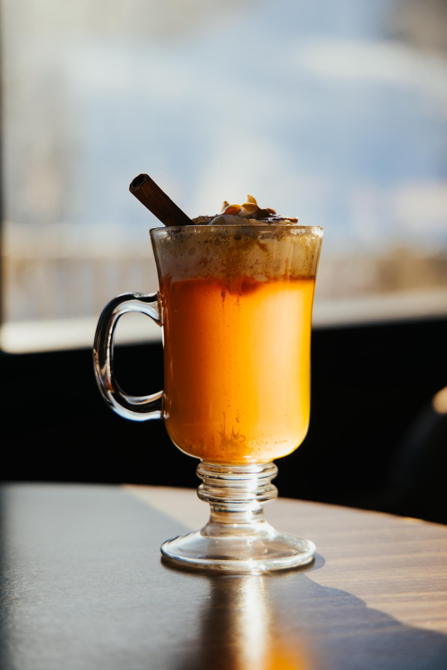 A latte with cinnamon stick in a glass mug, warmly lit.