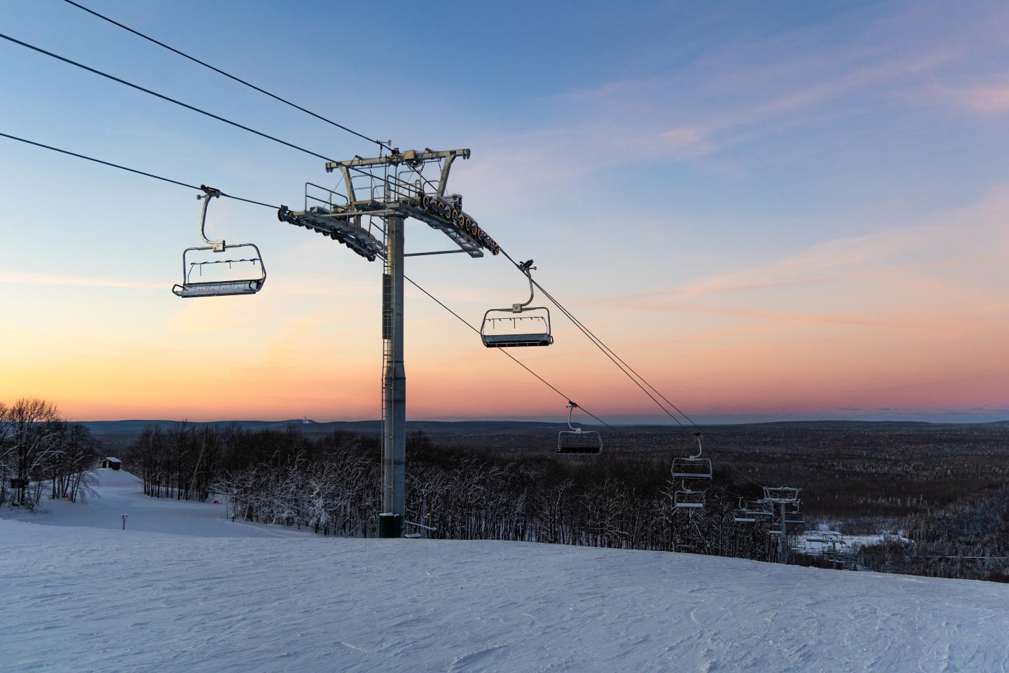 Ski lift over snowy slopes at sunset, with a colorful sky.