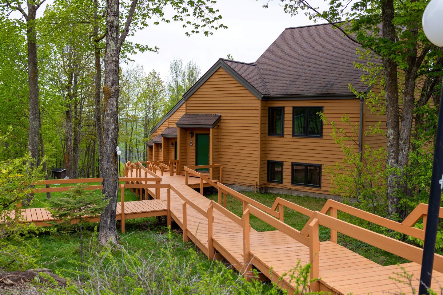 Wooden house with a wheelchair ramp surrounded by green trees.