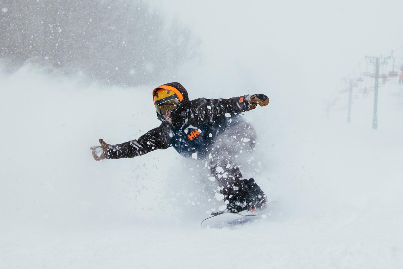 Snowboarder carving through fresh snow on a misty mountain slope.