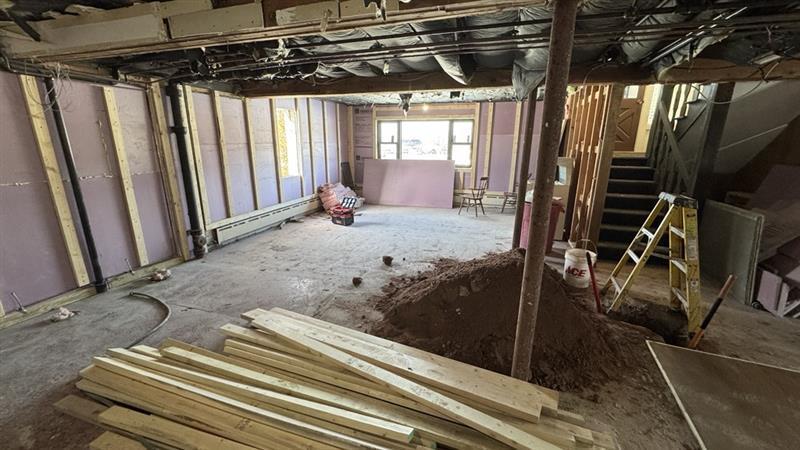 Basement under renovation with wooden beams and dirt piles, ladder near stairs.