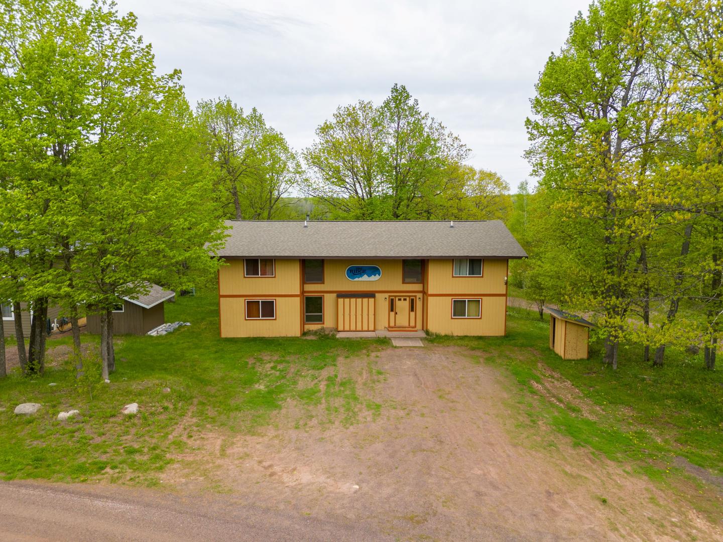 Two-story tan house surrounded by lush green trees.