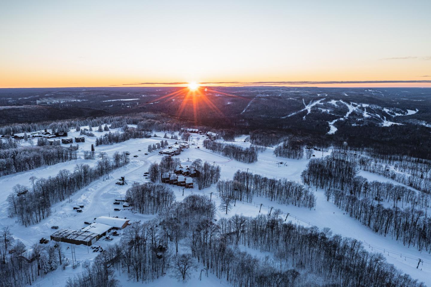 Snowy landscape at sunset, with winding roads and trees.