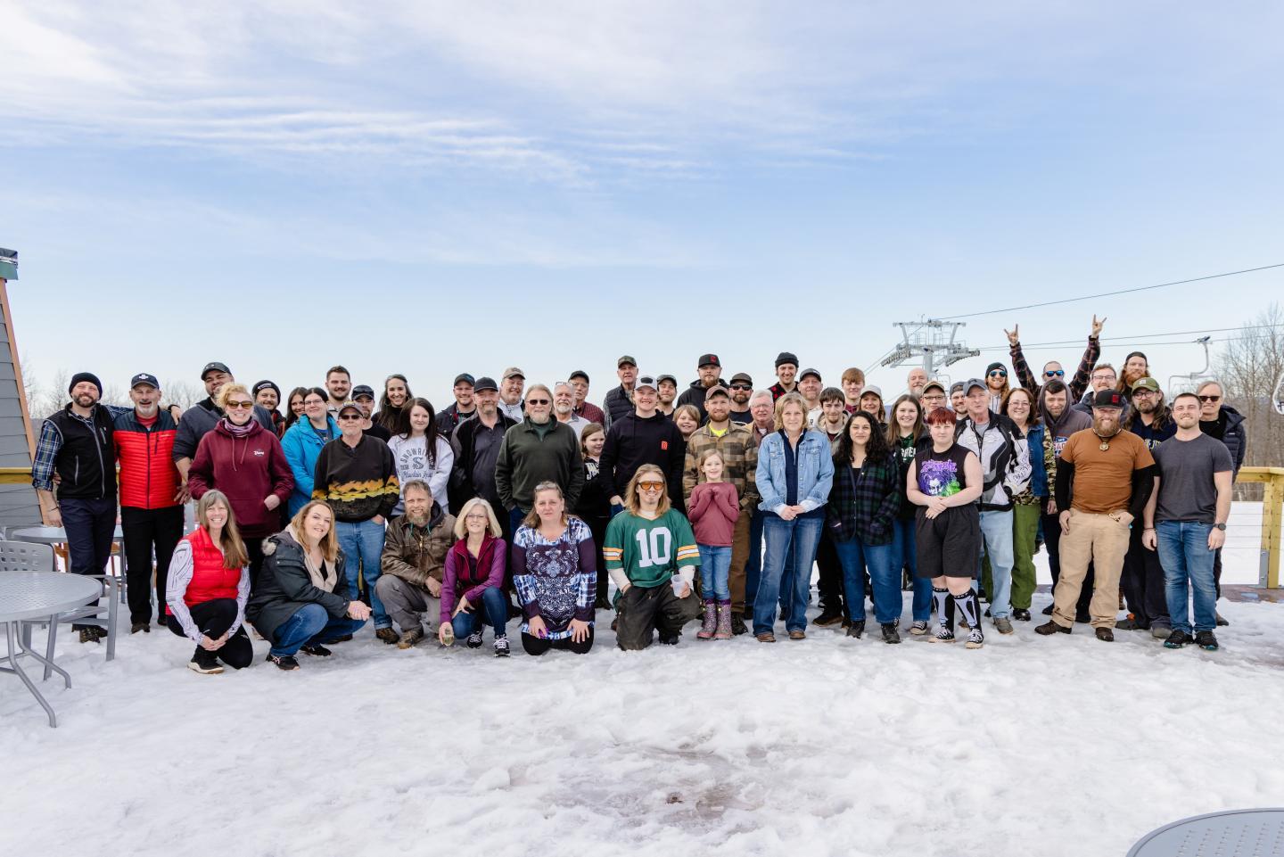 A large group of people pose on snow under a clear sky.