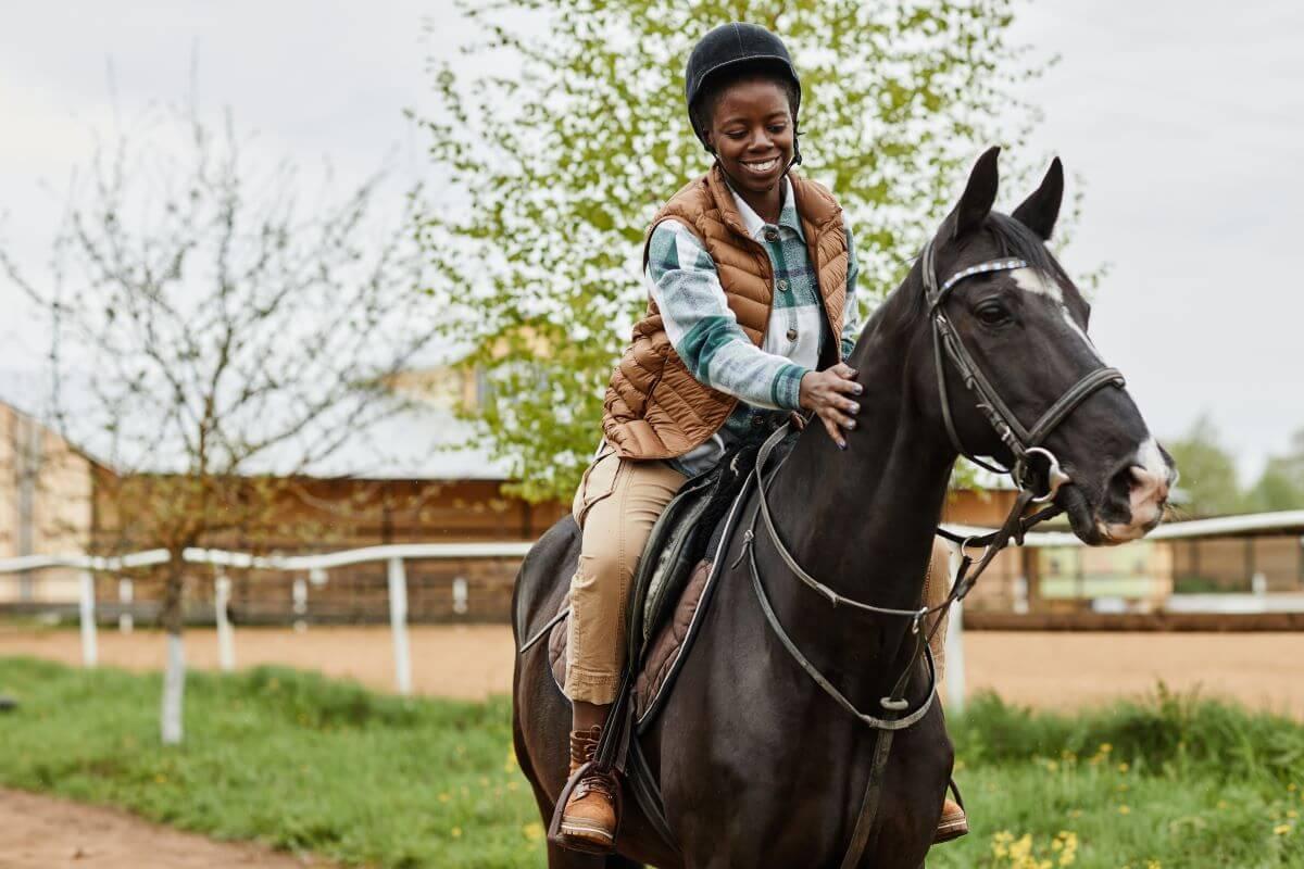 Person riding a black horse on a sunny day at a ranch.