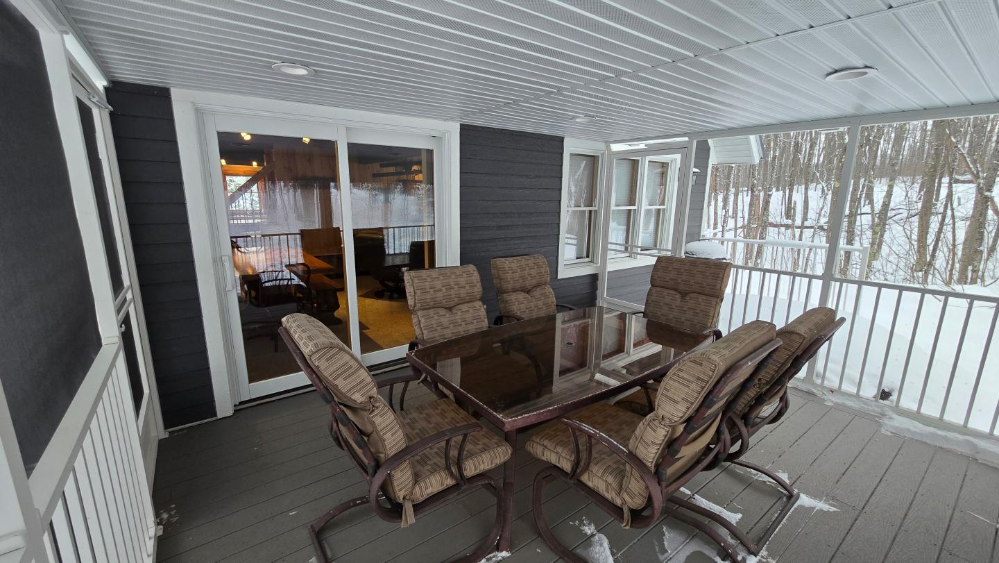 Covered porch with glass table and six chairs, snowy yard visible outside.