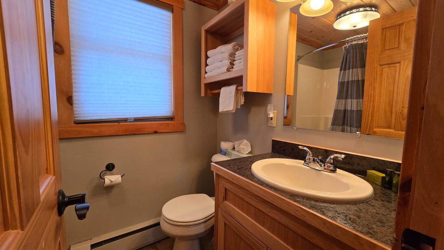 Compact bathroom with wooden cabinets, sink, toilet, and towels on shelves.