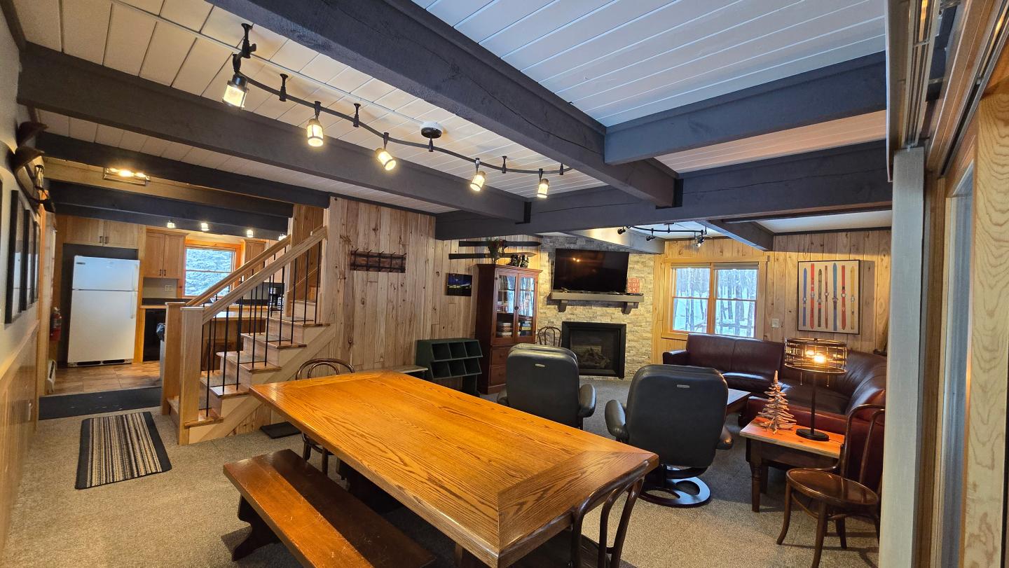 Cozy living room with wooden walls, large table, fireplace, and recliners.