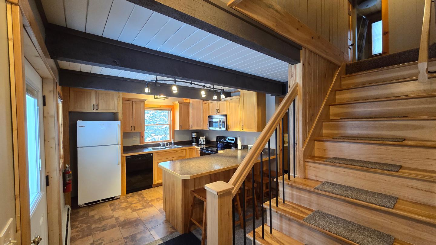 Wooden kitchen with white appliances, stone floor, and wooden stairs to the right.
