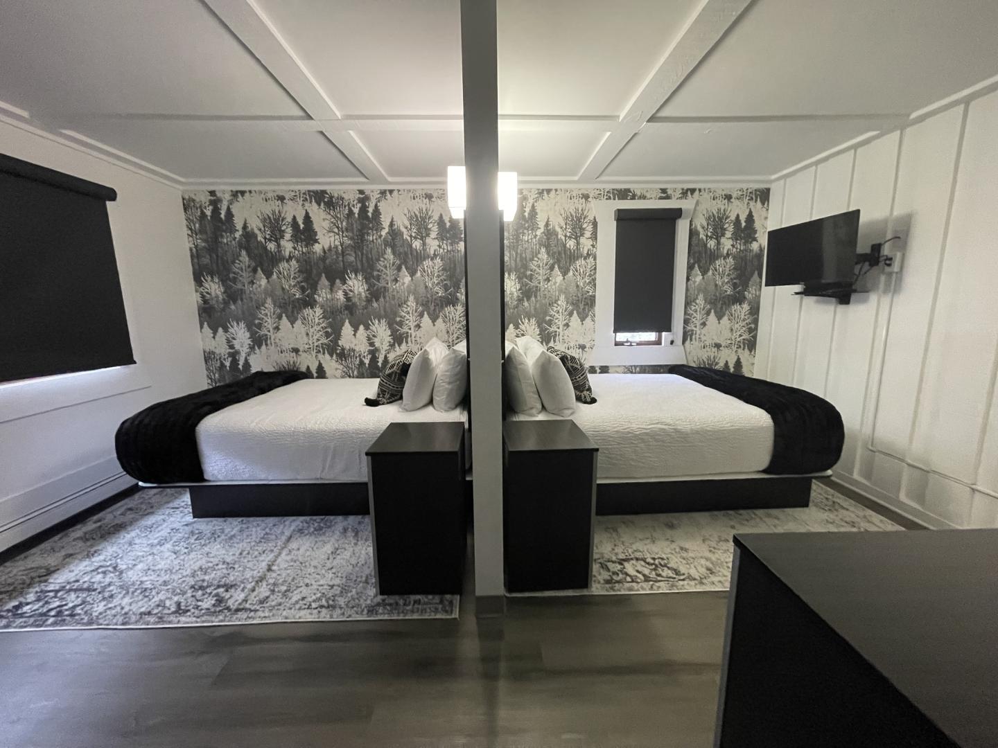 Modern bedroom with two beds separated by a partition, patterned wallpaper, and a wall-mounted TV.