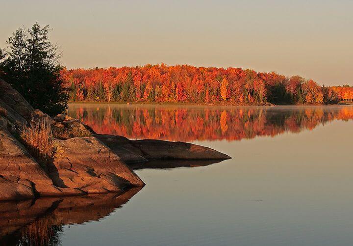 Calm lake reflecting vibrant autumn trees and rocky shore.